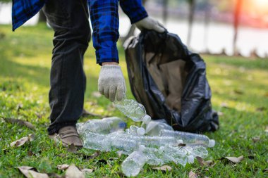 Hand picks up plastic bottles up close with young man volunteering to collect plastic bottles in garbage bags for environmental protection in the ecological forest background. recycling concept