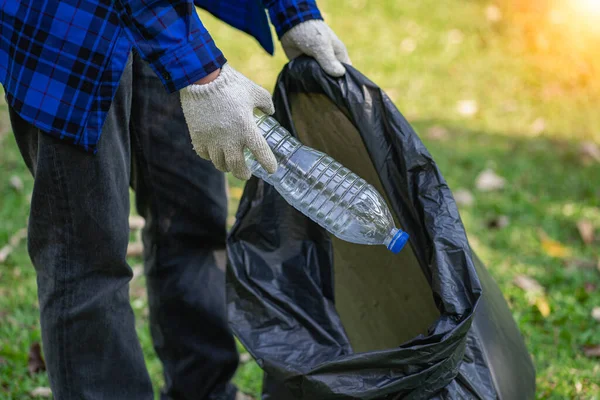 Hand picks up plastic bottles up close with young man volunteering to collect plastic bottles in garbage bags for environmental protection in the ecological forest background. recycling concept