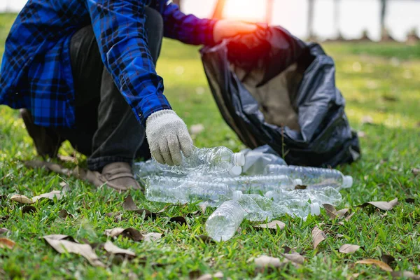 Hand picks up plastic bottles up close with young man volunteering to collect plastic bottles in garbage bags for environmental protection in the ecological forest background. recycling concept