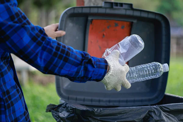 Hand picks up plastic bottles up close with young man volunteering to collect plastic bottles in garbage bags for environmental protection in the ecological forest background. recycling concept