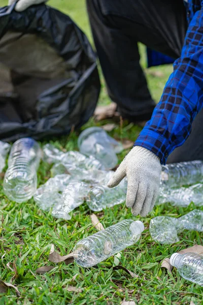 Hand picks up plastic bottles up close with young man volunteering to collect plastic bottles in garbage bags for environmental protection in the ecological forest background. recycling concept