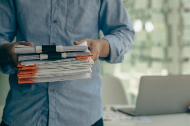 Young businessman standing in front of his desk holding many documents in office