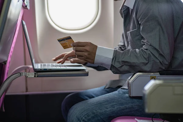 Asian young man sitting on plane pays online using credit card and laptop. online name ideas