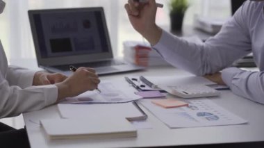 Caucasian woman discussing financial graphs in conference room with Asian colleagues, two business corners working together at a table discussing business projects. financial chart