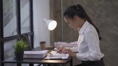 Asian woman accounting clerk working on paperwork in office at work Busy doing financial reports, calculations, documents. use a calculator, computer, notebook