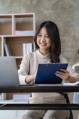 Online study using internet and technology Asian woman using laptop computer to work and study finance with graphs at home.