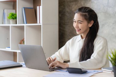 Online study using internet and technology Asian woman using laptop computer to work and study finance with graphs at home.