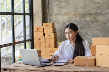 Starting a Successful Small Business Owner Independent Asian female saleswoman using laptop to check and Prepare parcel boxes to send to customers, SME entrepreneurs, online business ideas