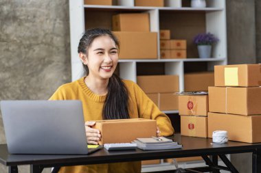 Starting a Successful Small Business Owner Independent Asian female saleswoman using laptop to check and Prepare parcel boxes to send to customers, SME entrepreneurs, online business ideas