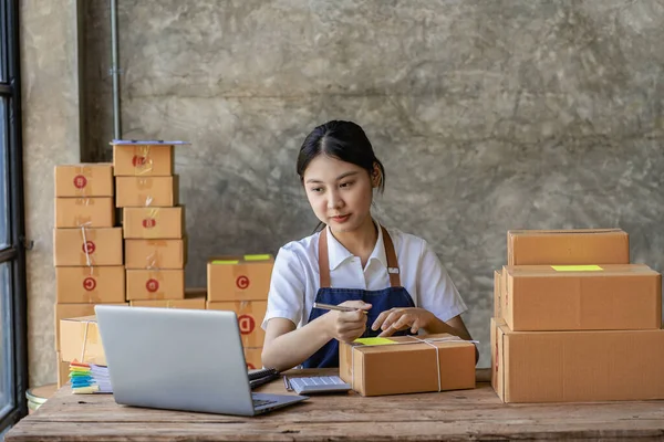 Starting a Successful Small Business Owner Independent Asian female saleswoman using laptop to check and Prepare parcel boxes to send to customers, SME entrepreneurs, online business ideas