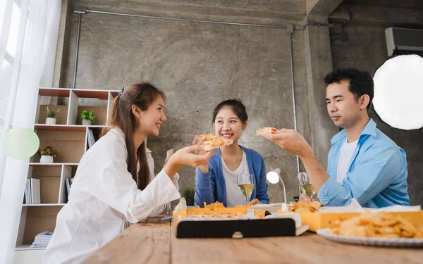 Young Asian male and female colleagues having lunch in the office eating pizza and communicating. The crew of young colleagues are having a pizza party together enjoying their free time.