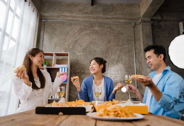 Young Asian male and female colleagues having lunch in the office eating pizza and communicating. The crew of young colleagues are having a pizza party together enjoying their free time.