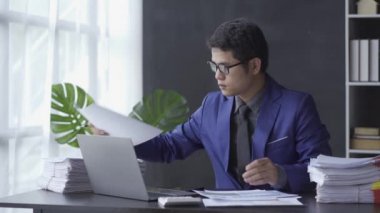Asian businessman focused on reviewing financial documents or working on paperwork in the office. Employee operators in suits are busy. 4k