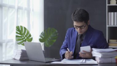 Asian businessman focused on reviewing financial documents or working on paperwork in the office. Employee operators in suits are busy. 4k