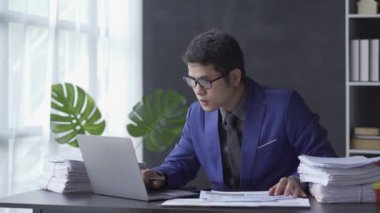 Asian businessman focused on reviewing financial documents or working on paperwork in the office. Employee operators in suits are busy. 4k