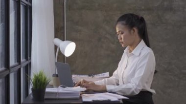 Young accountant working with graph papers. Close-up of an Asian woman using a laptop while working in the office.