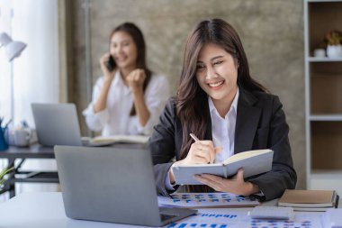 Two Asian women with laptop and financial graphs calculating accounting and taxes at the office. business idea