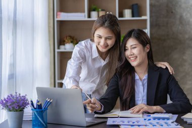Two Asian women with laptop and financial graphs calculating accounting and taxes at the office. business idea