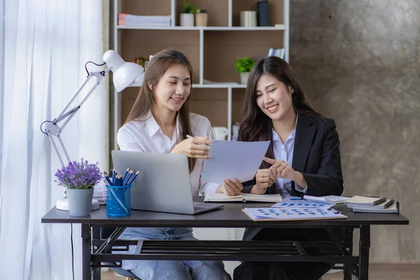 Two Asian women with laptop and financial graphs calculating accounting and taxes at the office. business idea