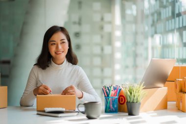 Small business startups, SME owners, Asian women entrepreneurs Successfully working with boxes and checking online orders with a laptop to prepare. Sell to customers. Online SME Business Ideas
