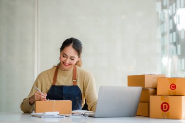 Small business startups, SME owners, Asian women entrepreneurs Successfully working with boxes and checking online orders with a laptop to prepare. Sell to customers. Online SME Business Ideas