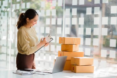 Small business startups, SME owners, Asian women entrepreneurs Successfully working with boxes and checking online orders with a laptop to prepare. Sell to customers. Online SME Business Ideas