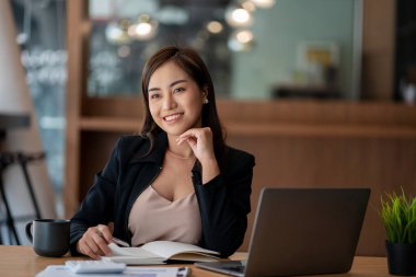 Dizüstü bilgisayar ve cep telefonuyla çalışan Asyalı bir iş kadını ya da muhasebeci. Mali belgelerinle masanda otururken gülümse ve mutlu ol. modern ofis hesap makinesi