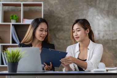 Two Asian business women working on a financial graph and a laptop.in the presentation and review of the business plan Joint financial marketing strategies in the meeting room with new employees in the office.