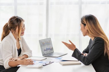 Two Asian business women working on a financial graph and a laptop.in the presentation and review of the business plan Joint financial marketing strategies in the meeting room with new employees in the office.