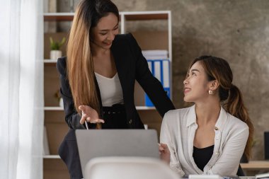 Two Asian business women working on a financial graph and a laptop.in the presentation and review of the business plan Joint financial marketing strategies in the meeting room with new employees in the office.