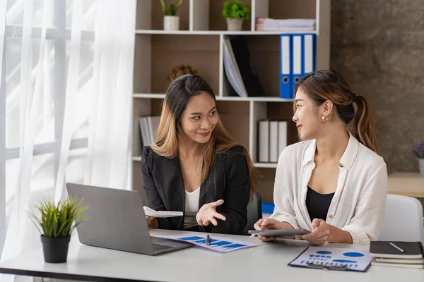 Two Asian business women working on a financial graph and a laptop.in the presentation and review of the business plan Joint financial marketing strategies in the meeting room with new employees in the office.