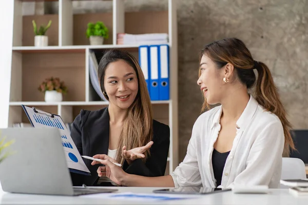 Two Asian business women working on a financial graph and a laptop.in the presentation and review of the business plan Joint financial marketing strategies in the meeting room with new employees in the office.