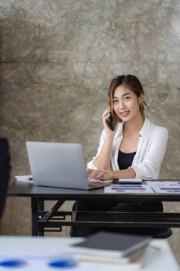 Beautiful Asian woman working and typing on laptop computer with smartphone in office. business woman looking at financial statistics graph data analysis profit growth business concept