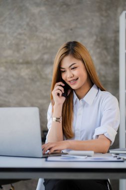 Asian woman working in office with laptop and financial documents with smartphone accounting concept