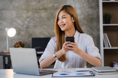 Asian woman working in office with laptop and financial documents with smartphone accounting concept