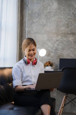 Smiling beautiful Asian woman working on a laptop sitting on the sofa at home online learning concept at home