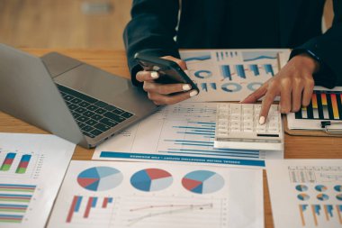 An accountant using a mobile smartphone while working analyzes business reports in the workplace. financial planning and accounting concepts