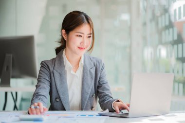 Beautiful Asian female accountant working on finance with business report and financial calculator concept.