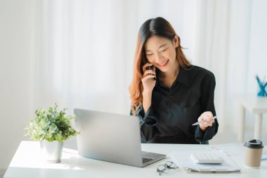 Young Asian businesswoman using calculator and laptop for math finance on wooden table, tax, accounting, statistical report.