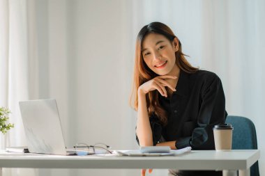 Young Asian businesswoman using calculator and laptop for math finance on wooden table, tax, accounting, statistical report.