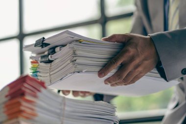 Businessman working in financial accounting with piles of documents on the desk at home work from home concept, business report, pile of unfinished paperwork