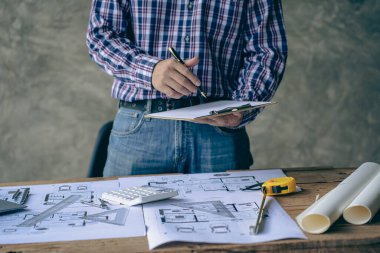 An engineer or architect working on a new project on a construction site. With blueprints and using a laptop draw a project design in the concept of an architectural engineer.