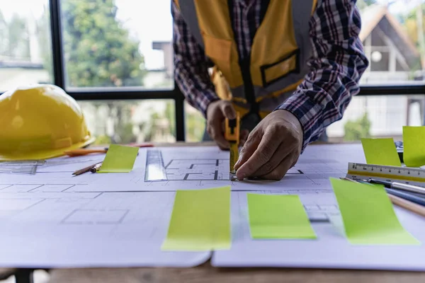 An engineer or architect working on a new project on a construction site. With blueprints and using a laptop draw a project design in the concept of an architectural engineer.