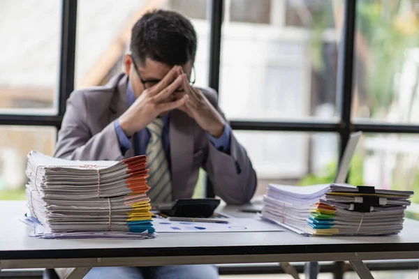 Businessman stressed with work with piles of unresolved documents on desk in office