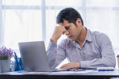 Young Asian businessman records income and expenses at home. Worried man. Serious while using notebook. Records, budgets, taxes, financial documents.