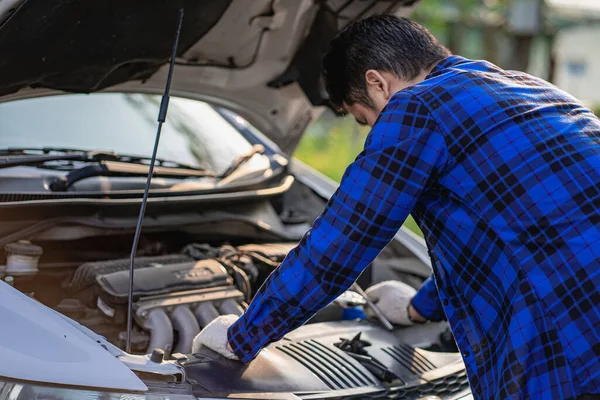 A serious Caucasian handsome young man looks at the engine of the car under the hood. To check something went wrong.