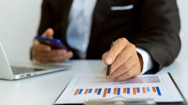 business man holding a smartphone and working on a laptop Trading graph data. Financial. Business works on his computer at his desk.
