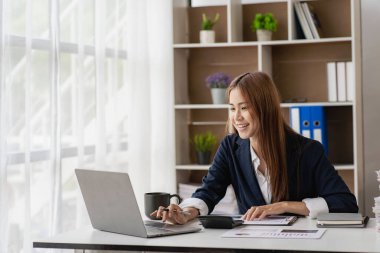 Charming Asian businesswoman or finance worker using a laptop computer and working on financial accounting reports in the office.
