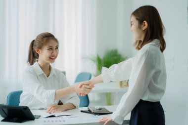 Two beautiful Asian women and an interviewer shake hands in a modern office. Business meeting, greeting, agreement. Concept after negotiation with her partner. Teamwork and Success Concept
