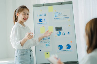 Two Asian women talk, discuss, work on the new start-up project idea. Analyze financial graphs, marketing plans and office investments.